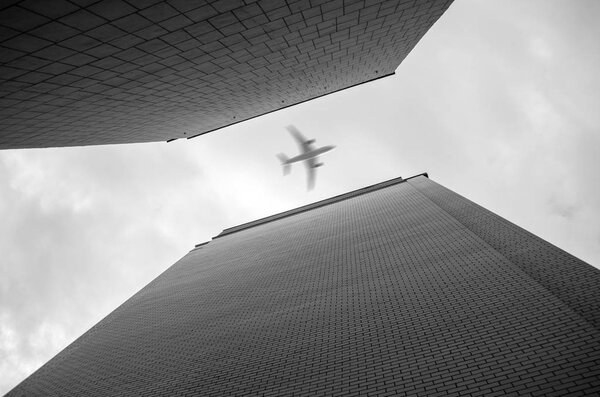 Airplane flying over skyscrapers. Bottom-up view. Black and white photo.
