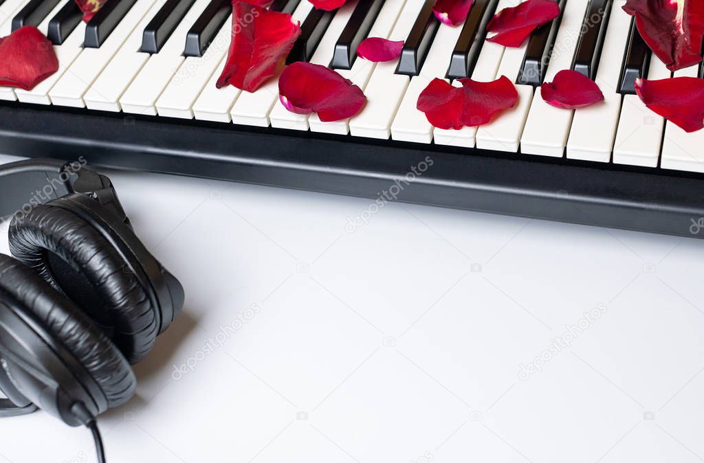 Piano keys strewn with red rose petals and headphones, isolated,
