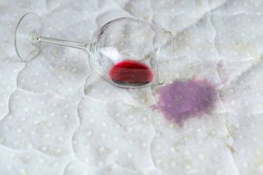 Wine glass spilled on bed. Dropped wineglass on white bed sheet.