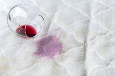 Wine glass spilled on bed. Dropped wineglass on white bed sheet.