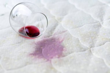 Wine glass spilled on bed. Dropped wineglass on white bed sheet.