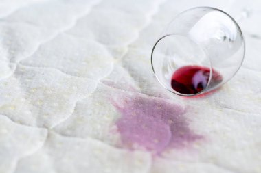 Wine glass spilled on bed. Dropped wineglass on white bed sheet.