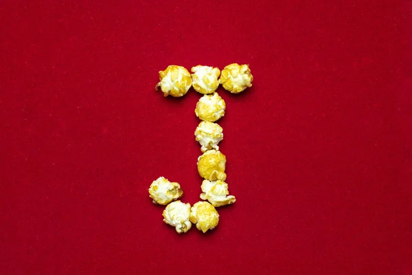 Английский алфавит из кинопопкорна. Буква J. Красный фон f — стоковое фото