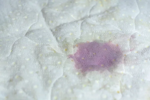 Wet stain of spilled red wine on bed. Red wine stain on white be