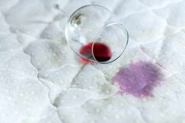 Copo de vinho derramado na cama. Vinho caído em lençol branco . — Fotografia de Stock