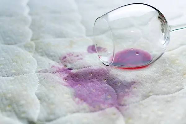 Copo de vinho derramado na cama. Vinho caído em lençol branco . — Fotografia de Stock