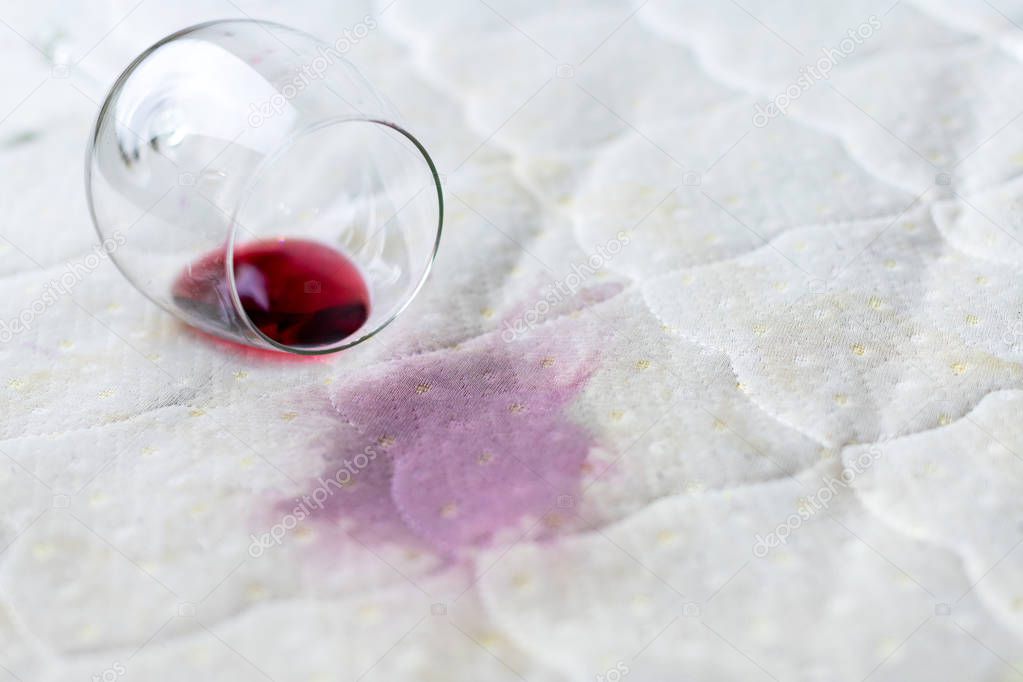 Wine glass spilled on bed. Dropped wineglass on white bed sheet.