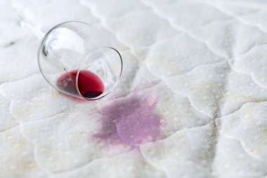 Wine glass spilled on bed. Dropped wineglass on white bed sheet.