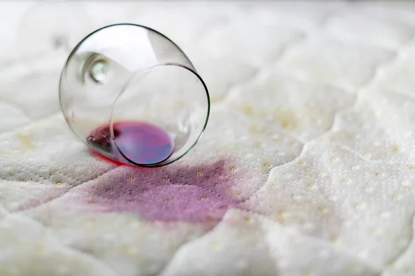 Copo de vinho derramado na cama. Vinho caído em lençol branco. Mancha cor-de-rosa. Situação infeliz e infeliz . — Fotografia de Stock