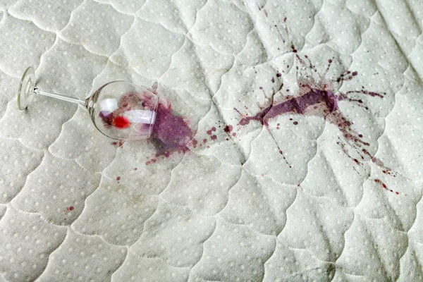 Copo de vinho derramado na cama. Acidentalmente deixou cair vinho no lençol branco. Uma situação infeliz e infeliz. Mancha molhada . — Fotografia de Stock