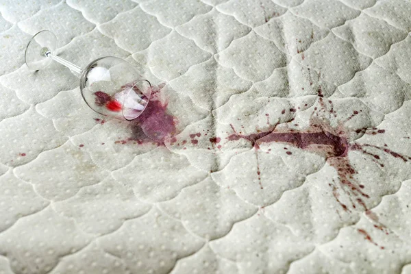 Vaso de vino derramado en la cama. Accidentalmente dejó caer la copa de vino en la sábana blanca. Una situación desafortunada. Mancha húmeda . — Foto de Stock