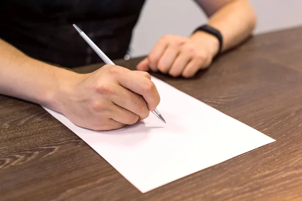 Empresário sentado à mesa e segura caneta na mão direita. Há uma folha de papel em branco na mesa. Fotografia de conceito . — Fotografia de Stock