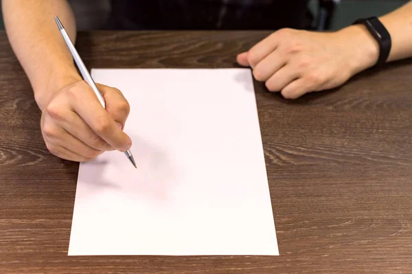Obchodník sedí u stolu a drží pero v pravé ruce. Na stole je prázdný list papíru. Koncept, fotografie. — Stock fotografie