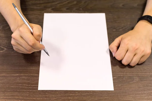 Empresário sentado à mesa e segura caneta na mão direita. Há uma folha de papel em branco na mesa. Fotografia de conceito . — Fotografia de Stock