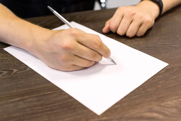 Empresário sentado à mesa e segura caneta na mão direita. Há uma folha de papel em branco na mesa. Fotografia de conceito . — Fotografia de Stock
