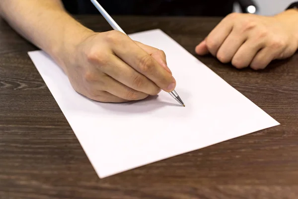 Empresário sentado à mesa e segura caneta na mão direita. Há uma folha de papel em branco na mesa. Fotografia de conceito . — Fotografia de Stock