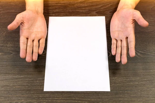 Obchodník sedí u stolu. Na stole je prázdný list papíru. Nepochopení gesto rukama. Koncept, fotografie. — Stock fotografie