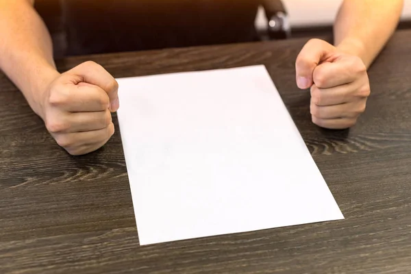 Empresario sentado en la mesa. Hay una hoja de papel en blanco sobre la mesa. Un gesto de enojo con las manos. Concepto foto . —  Fotos de Stock