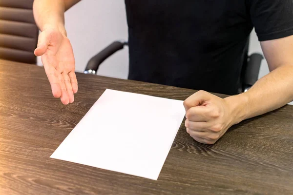 Empresario sentado en la mesa. Hay una hoja de papel en blanco sobre la mesa. Un gesto de enojo con las manos. Concepto foto . — Foto de Stock