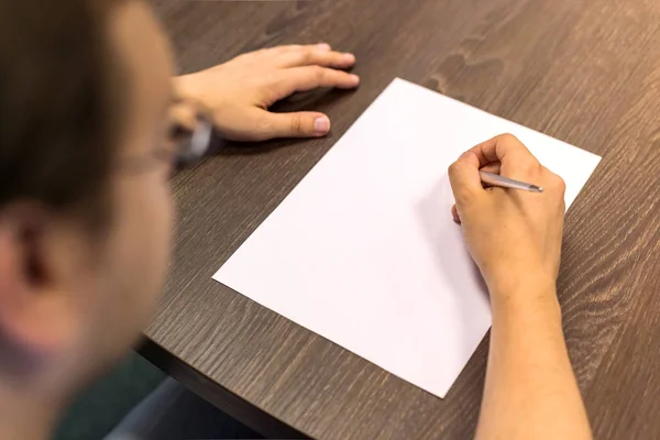 Empresario sentado en la mesa y sostiene la pluma en la mano derecha. Hay una hoja de papel en blanco sobre la mesa. Concepto foto . —  Fotos de Stock