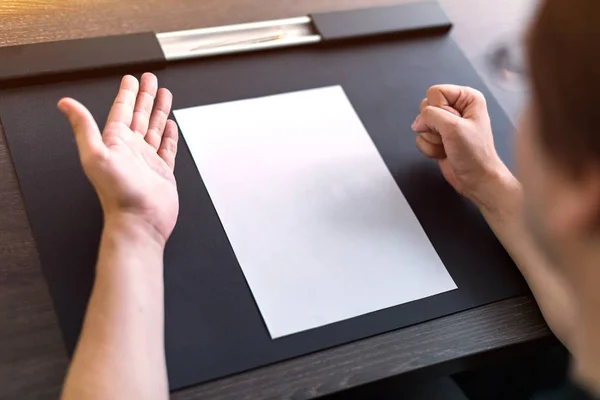 Üzletember ül az asztalnál. A táblán üres papírlap van. Dühös gesztus kézzel. Koncepció fotó. — Stock Fotó