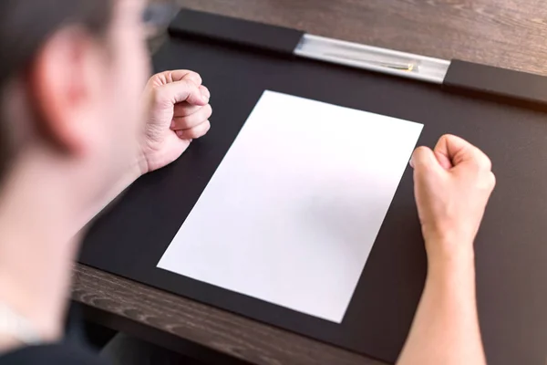 Empresário sentado à mesa. Há uma folha de papel em branco na mesa. Um gesto de raiva com as mãos. Fotografia de conceito . — Fotografia de Stock