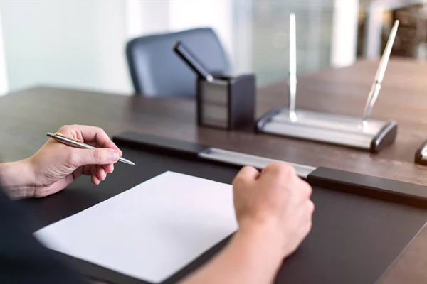 Empresario sentado en la mesa y sostiene la pluma en la mano izquierda. Hay una hoja de papel en blanco sobre la mesa. Un gesto de enojo con las manos. Concepto foto . —  Fotos de Stock