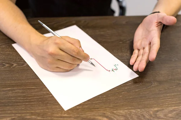 Empresário sentado à mesa e segura caneta na mão direita. Há uma folha de papel com um gráfico de negociação na mesa. Fotografia de conceito . — Fotografia de Stock