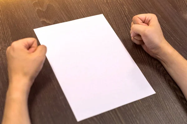 Empresário sentado à mesa. Há uma folha de papel em branco na mesa. Um gesto de raiva com as mãos. Fotografia de conceito . — Fotografia de Stock