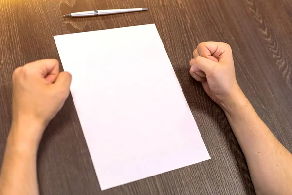 Empresário sentado à mesa. Há uma folha de papel em branco na mesa. Um gesto de raiva com as mãos. Fotografia de conceito . — Fotografia de Stock