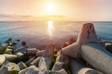 Beautiful sunset seascape. Breakwaters tetrapods ashore of pier. Cargo ships on the horizon. Travel dreams and motivation clipart