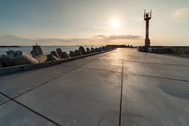 North pier with breakwaters, sunset seascape. Tetrapods along edges of pier. Beautiful evening seascape. Modern lighthouse in sunlight. clipart