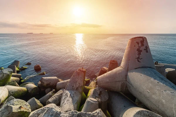 Bela paisagem do pôr-do-sol. Quebra-mares tetrápodes em terra de cais. Navios de carga no horizonte. Sonhos de viagem e motivação — Fotografia de Stock