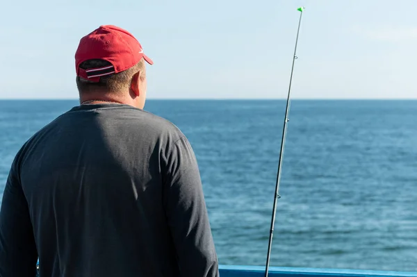 Ψαράς που ψαρεύει από την προβλήτα. Ένας άνθρωπος με καλάμι ψαρέματος με κόκκινο καπάκι. Ο καιρός του ανέμου, ήρεμος. Αντιγραφή χώρου. Πλούσια αλιεύματα, ψάρι μέρος. — Φωτογραφία Αρχείου