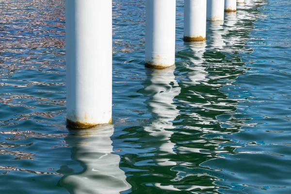 Rusty pier posts in salt sea water. White columns diagonal. Pillars mount for bridge. Sunny weather. — Stock Photo, Image