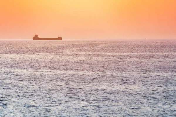 Little tugboat and big cargo ship. Beautiful sunset over sea. Br