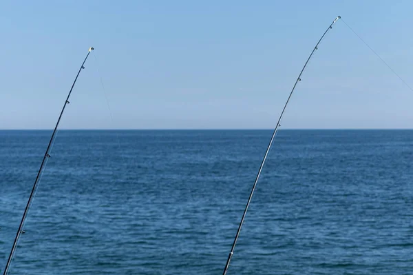 Two fishing rod against blue ocean or sea background, copy space. Waiting for biggest haul. Meditative relax sport.