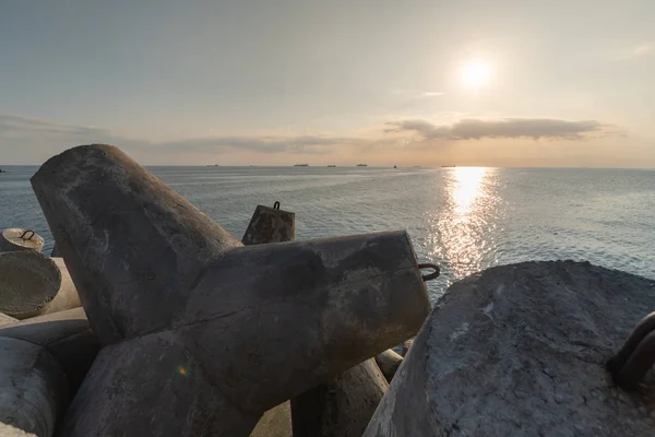 Bela paisagem do pôr-do-sol. Sonhos de viagem e motivação. Quebra-mar tetrápodes na costa do cais. Navios de carga no horizonte . — Fotografia de Stock