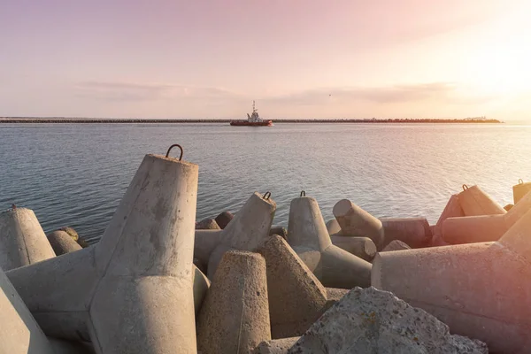 Gemi römorkör limana kargo gemisi çekme için yüksek denizlerde gider. İskelenin üzerinde güzel gün batımı. Tetrapod ara suları limanda.