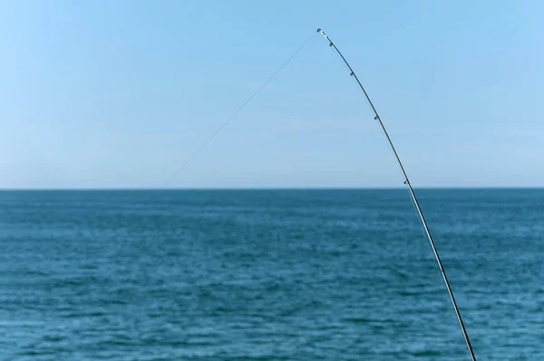 Caña de pescar contra el océano azul o fondo marino, espacio de copia. Esperando el transporte más grande. Deporte relajante meditativo . — Foto de Stock