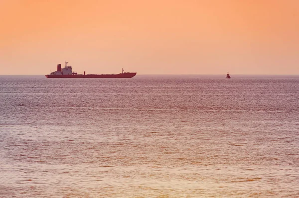 Küçük römorkör ve büyük kargo gemisi. Deniz üzerinde güzel gün batımı. Nefes kesen seyahat görünümü, kopyalama alanı.