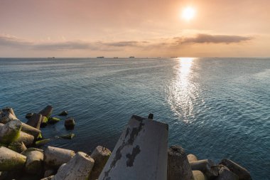 Güzel gün batımı deniz manzarası. Seyahat hayalleri ve motivasyon. Rıhtım kıyısındaki kırılma suları tetrapodları. Ufukta kargo gemileri.