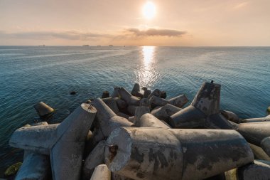 Beautiful sunset seascape. Travel dreams and motivation. Breakwaters tetrapods on shore of pier. Cargo ships on the horizon. clipart