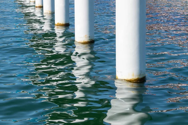 Rusty pier posts in salt sea water. White columns diagonal. Pillars mount for bridge. Sunny weather. — Stock Photo, Image