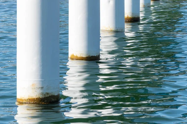 Canais enferrujados em água salgada do mar. Colunas brancas diagonais. Pilares montados para ponte. Tempo ensolarado . — Fotografia de Stock