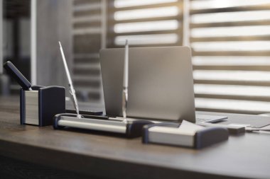 Modern ofis işyeri. İş yerinde şef, patron ya da diğer çalışanlar için iş bilgisayarı var. Defter çalışma masasında. Ofis büyük bir şirket. Işıklar yarı açık panjurlarda.