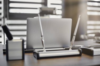 Modern ofis işyeri. İş yerinde şef, patron ya da diğer çalışanlar için iş bilgisayarı var. Defter çalışma masasında. Ofis büyük bir şirket. Işıklar yarı açık panjurlarda.