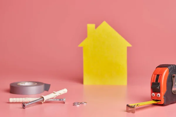 Metal Tape intézkedés vicces fogalom. Ház felújítása. Home javítási és felújított koncepció. Sárga ház alakú alak rózsaszín háttér. — Stock Fotó