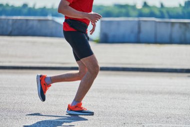 Koşan adam. Şehir yolunda spor kıyafetleriyle koşan atletik bir adam. Sağlıklı yaşam tarzı, spor hobisi. Sokak çalışması, açık hava koşusu.