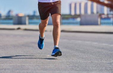 Koşan adam. Şehir yolunda spor kıyafetleriyle koşan atletik bir adam. Sağlıklı yaşam tarzı, spor hobisi. Sokak çalışması, açık hava koşusu.